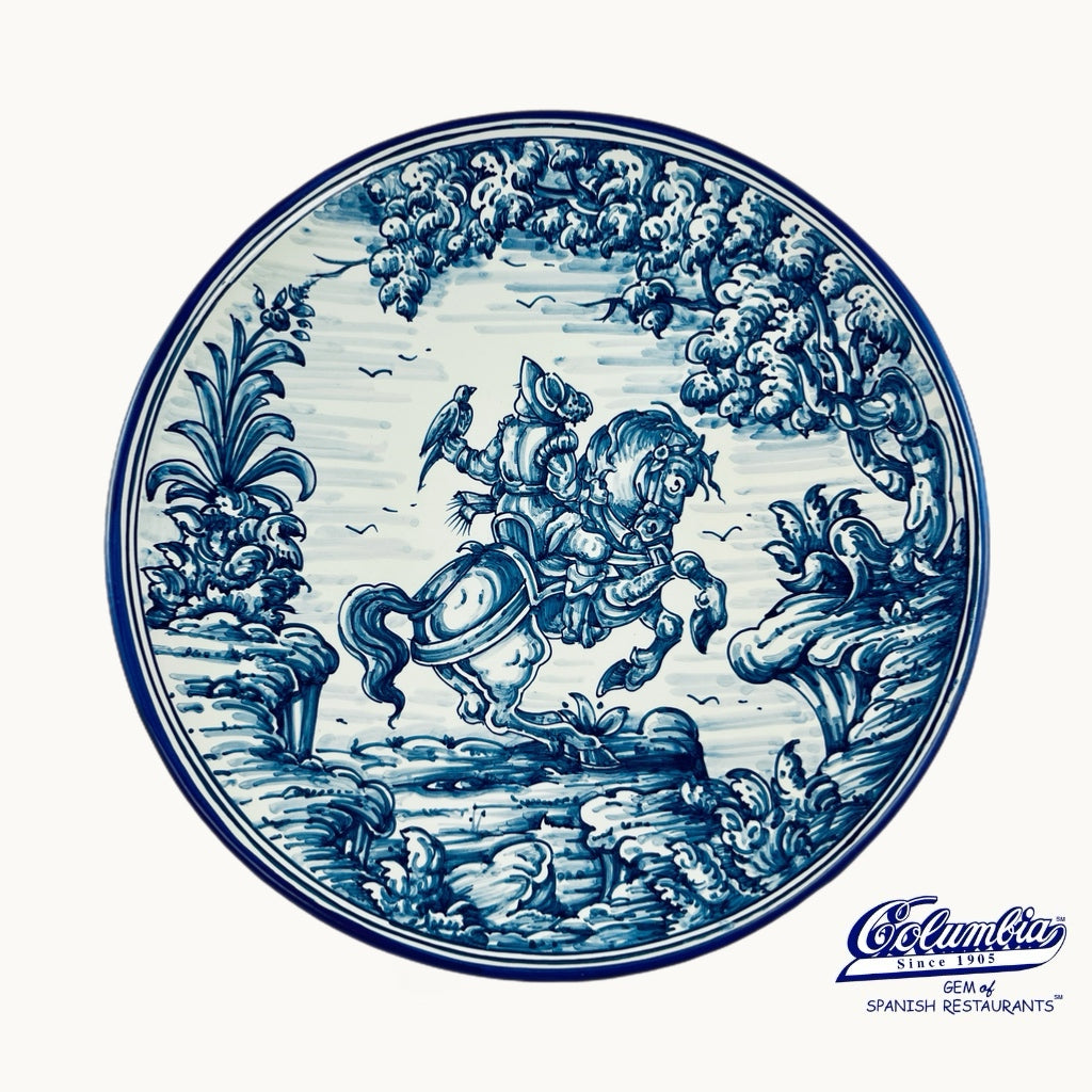 Decorative plate with blue and white floral and animal design, featuring a brand logo at the bottom.
