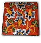 A square ceramic plate with a red background and a multicolor floral pattern.
