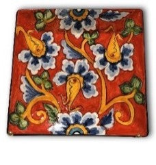 A square ceramic plate with a red background and a multicolor floral pattern.