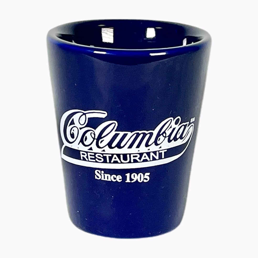 A blue shot glass with the Columbia Restaurant logo printed on it.