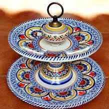 A two-tiered serving tray with brightly colored floral and geometric patterns on a red background, with a black handle on top.