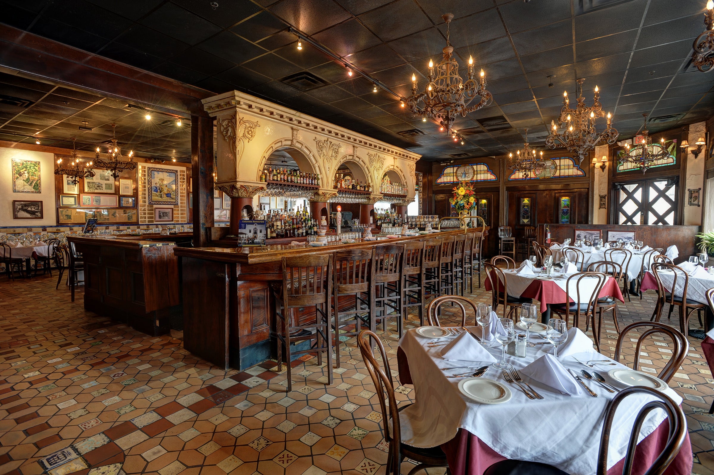 Elegant interior of Columbia Restaurant with ornate wooden bar, arched mirrors, chandeliers, tiled floors, and tables set with white tablecloths and place settings