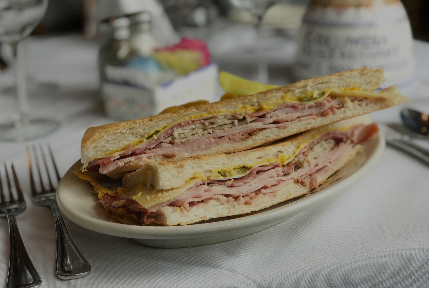 Half-cut Cuban sandwich on a plate with cutlery and a blurred background