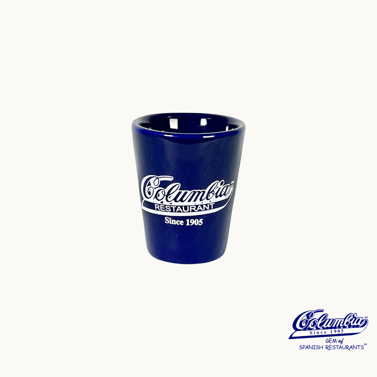 A blue ceramic shot glass with the white text 'Columbia Restaurant' and the logo 'Colombia' printed on it.